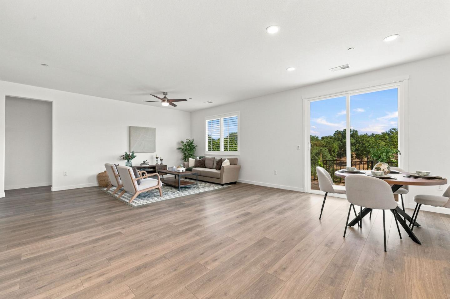 Open-plan living and dining room with wood-look floors and sliding doors to a tree-lined balcony.