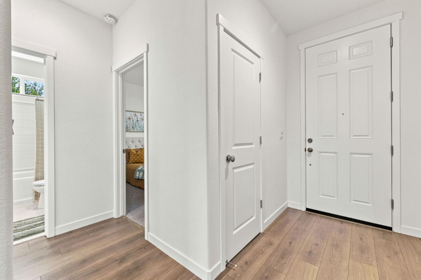 Entry foyer with a white paneled front door, wood-look flooring, and adjoining bathroom and bedroom doorways.