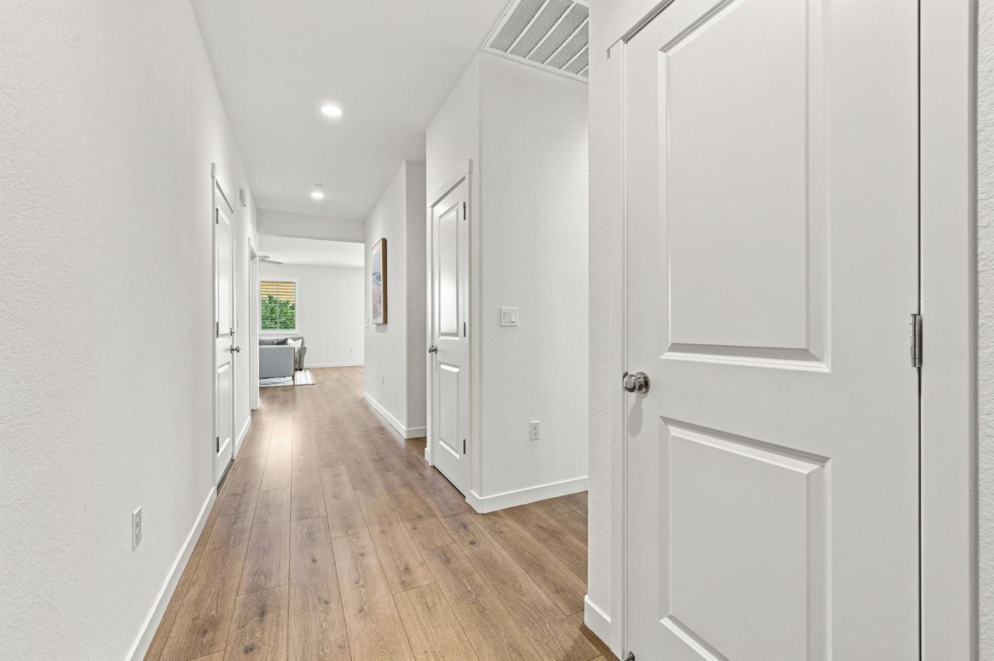 Bright hallway with wood-look flooring and white paneled doors, opening onto a furnished living room.