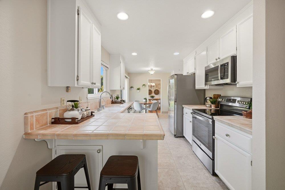 Kitchen with white cabinets, stainless steel appliances, and a tiled counter with two dark stools.