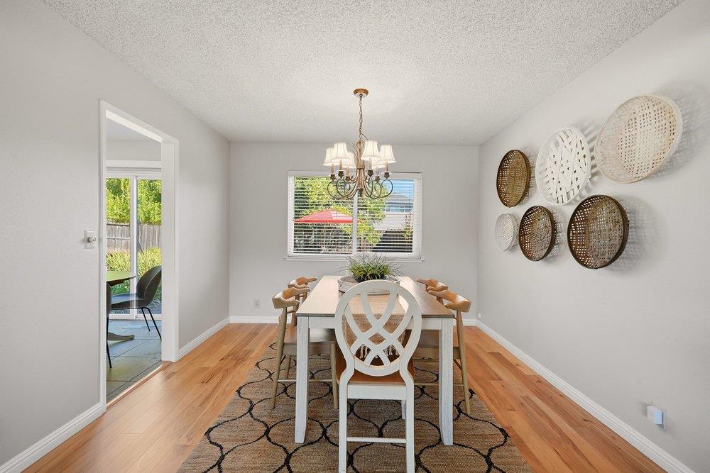 Dining room with a white table, patterned rug, chandelier, and woven wall decorations.