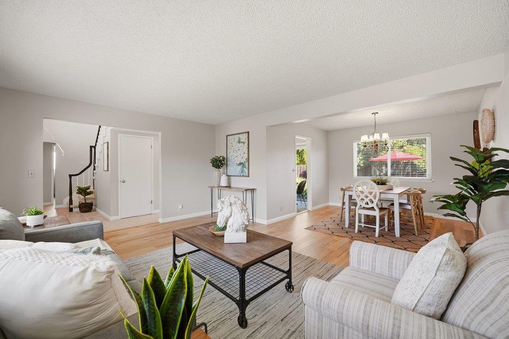 Open-plan living and dining room with light wood floors, a gray sectional, and a staircase.