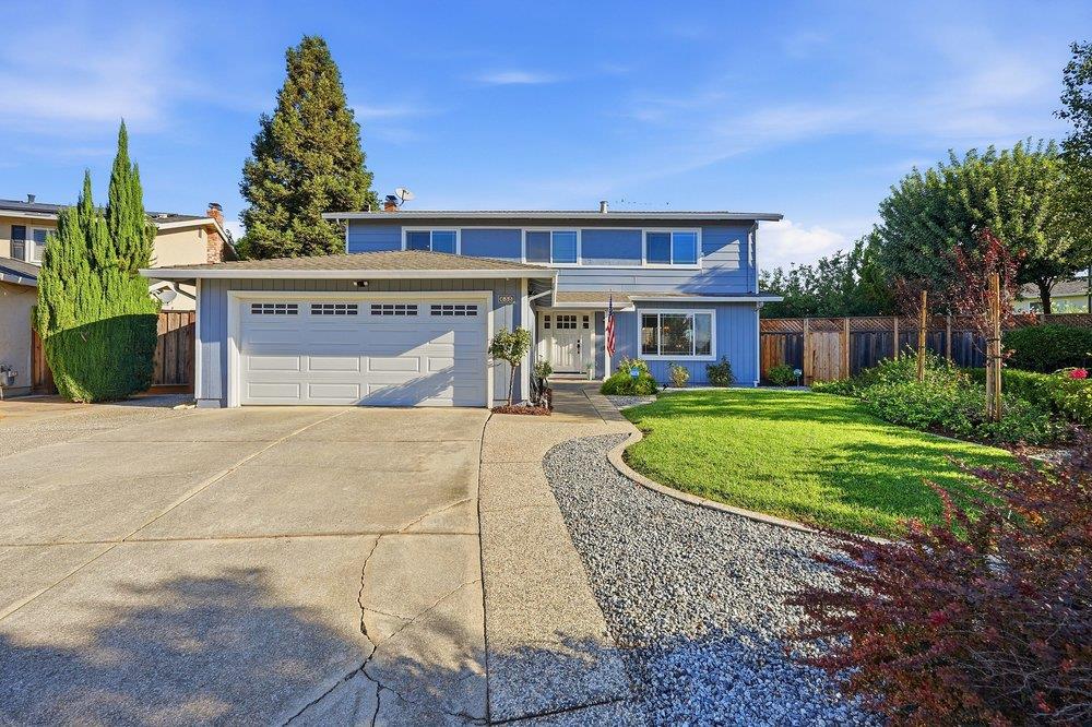 Two-story blue house with a double garage, broad driveway, and curved gravel garden border.