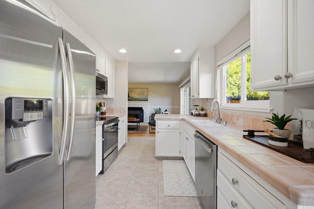 Bright kitchen with stainless steel appliances, pale tile counters, and a window overlooking greenery.