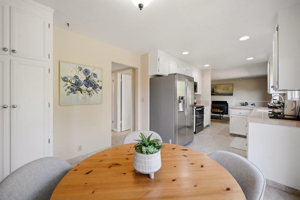 Kitchen with white cabinets and stainless appliances, viewed past a round wooden dining table.