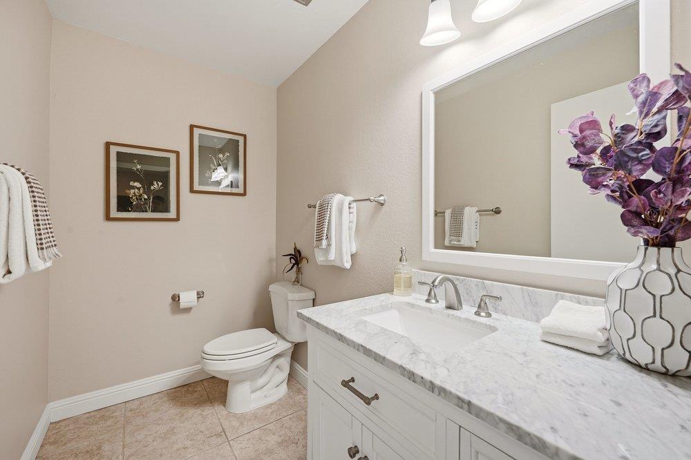 Bathroom with a white vanity, marble-look counter, large mirror, and purple foliage in a vase.