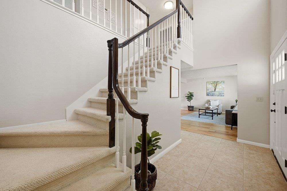 Entry foyer with a carpeted staircase, dark wood handrail, and view into a furnished living room.