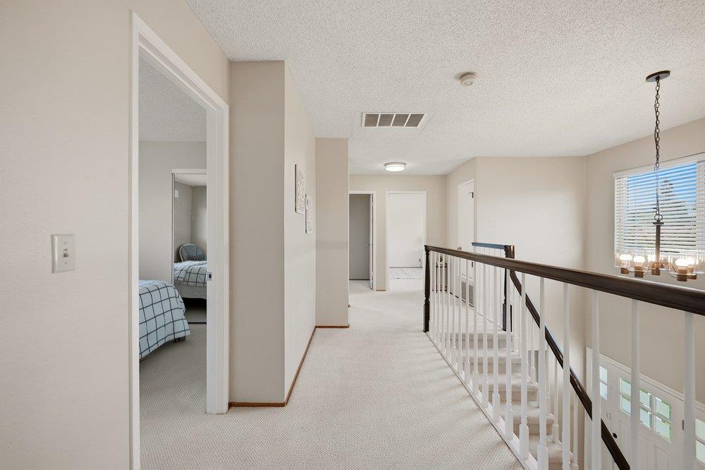 Carpeted upstairs hallway with a dark wood railing, bedroom doorways, and a window with blinds.