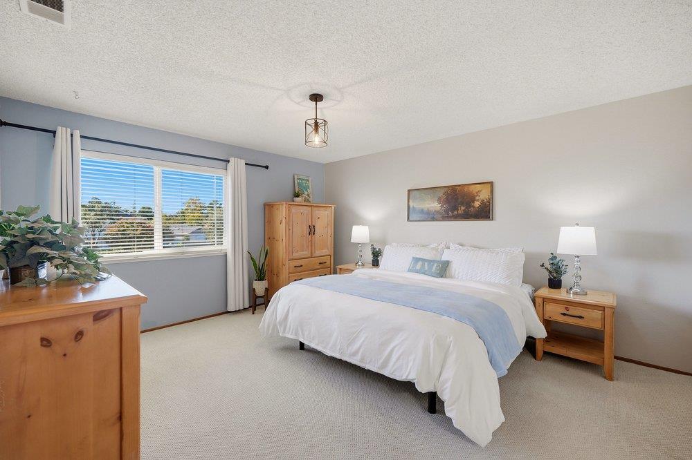 Staged bedroom with a white bed, pale blue throw, light wood furniture, and a large window.