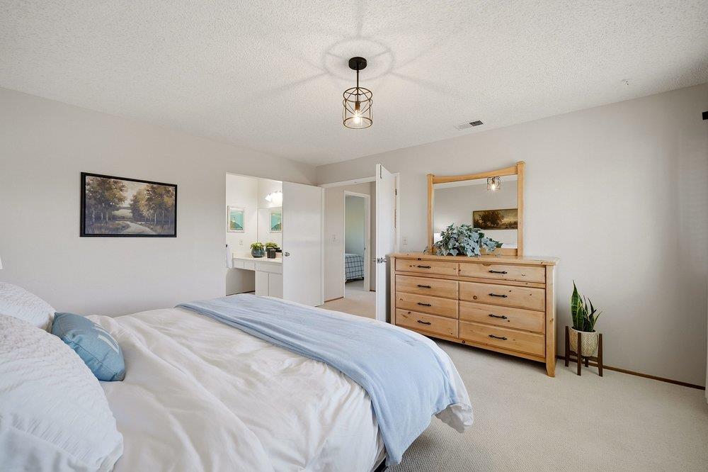 Bedroom with pale blue bedding, a light wood dresser and mirror, and an open doorway to the bathroom.