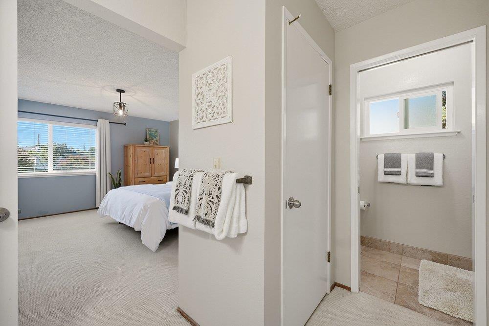 Bedroom with a white bed and wooden armoire beside an adjoining tiled bathroom.