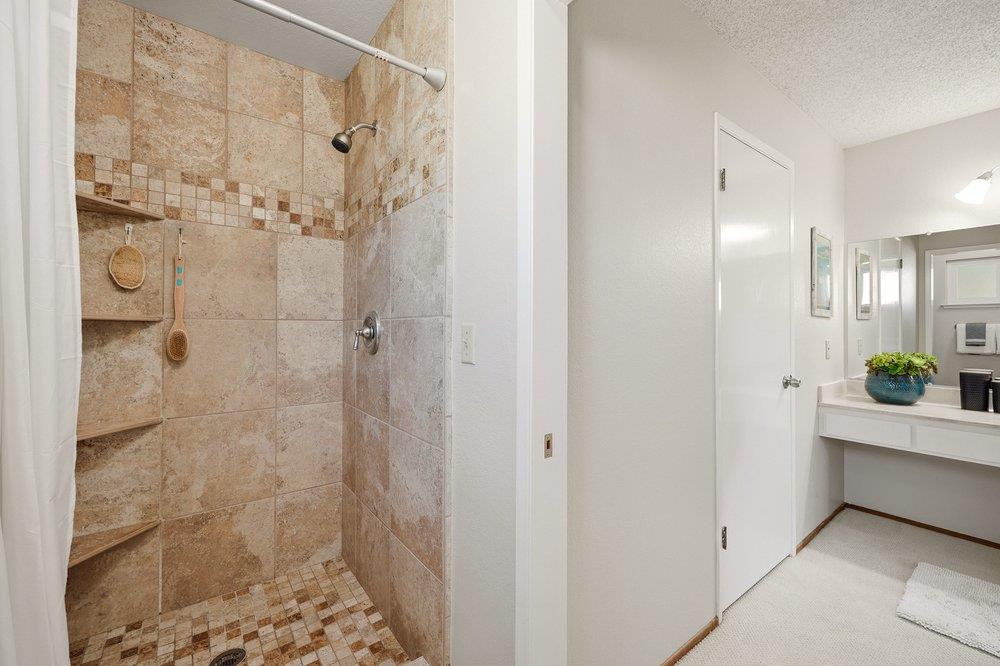 Bathroom with a tan tiled walk-in shower, built-in shelves, and a white vanity with mirrors.