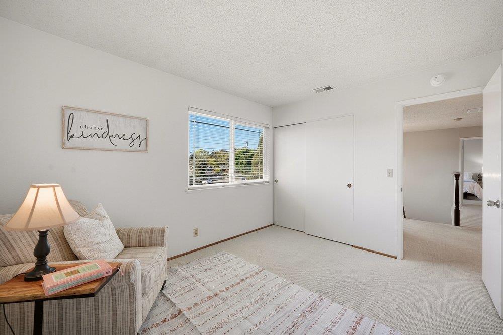 Sitting room with a striped sofa, patterned rug, and closet beside an open bedroom doorway.