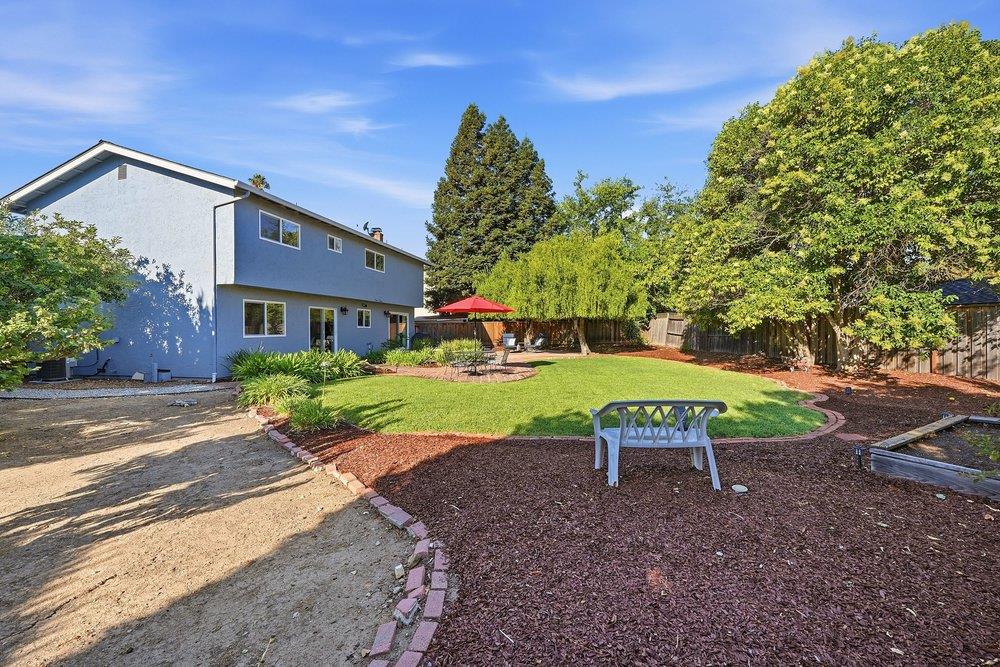 Two-story gray home overlooking a landscaped backyard with lawn, mature trees, and a red patio umbrella.