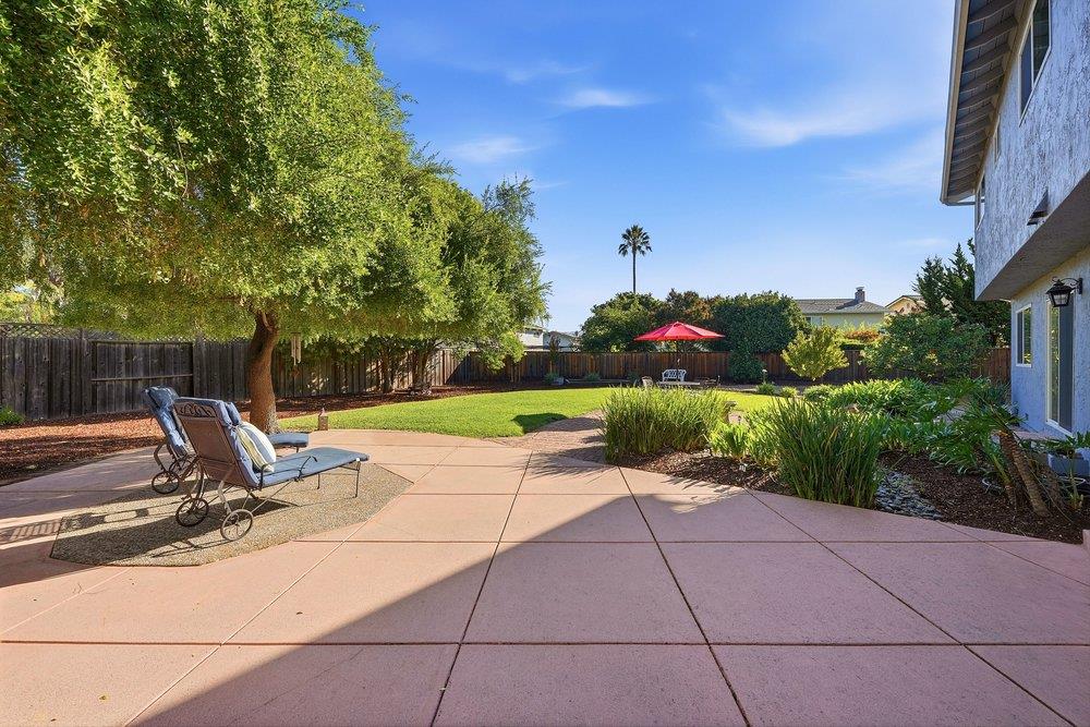 Backyard patio with reclining chairs, a green lawn, mature trees, and a red umbrella.