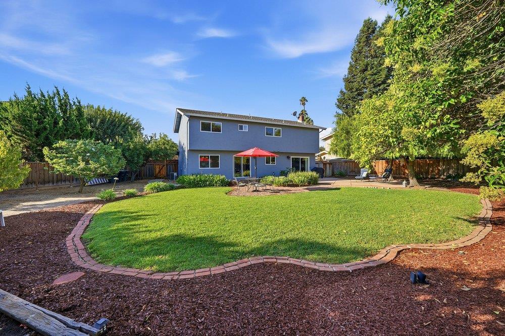 Two-story gray home behind a curved lawn, with mature trees and a red patio umbrella.