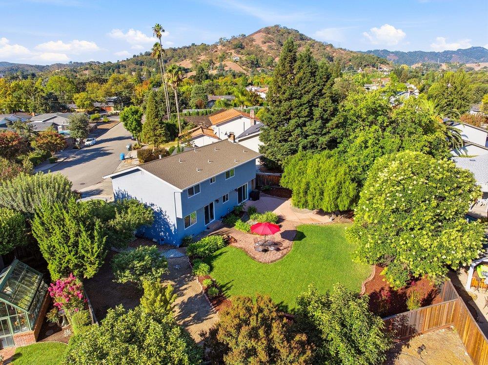 Aerial view of a home with a green backyard, patio umbrella, and surrounding hills.