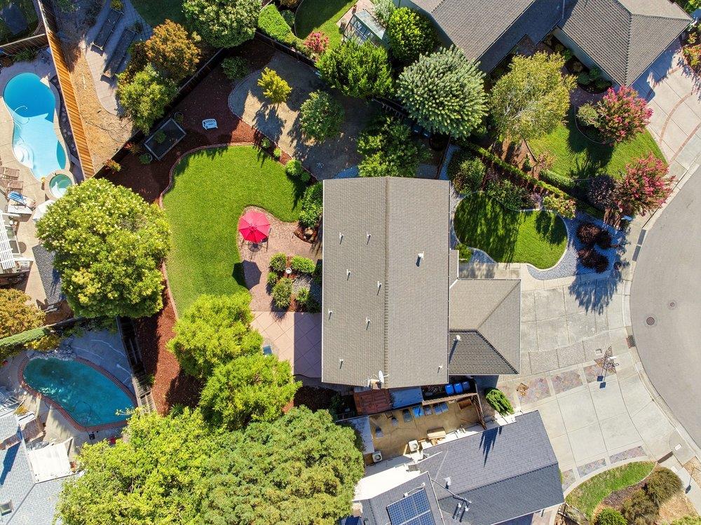 Aerial view of a landscaped home with a swimming pool, green lawn, and paved patio.