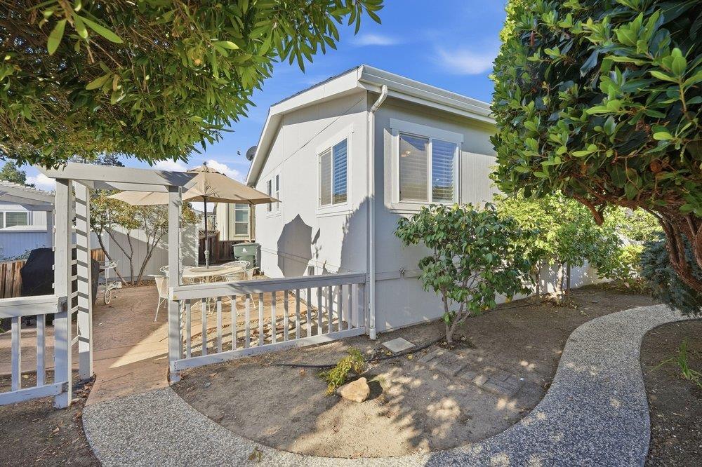 Light-colored home with a small deck and railing beside a shaded patio and pergola.