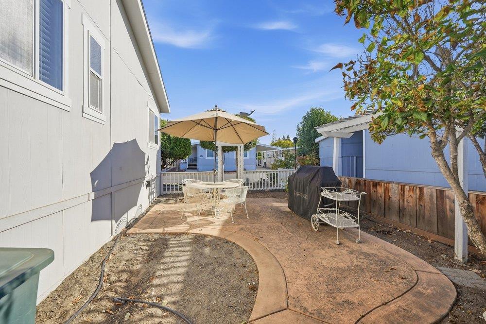 Backyard patio with a round table under an umbrella, a covered grill, and a decorative metal bench.