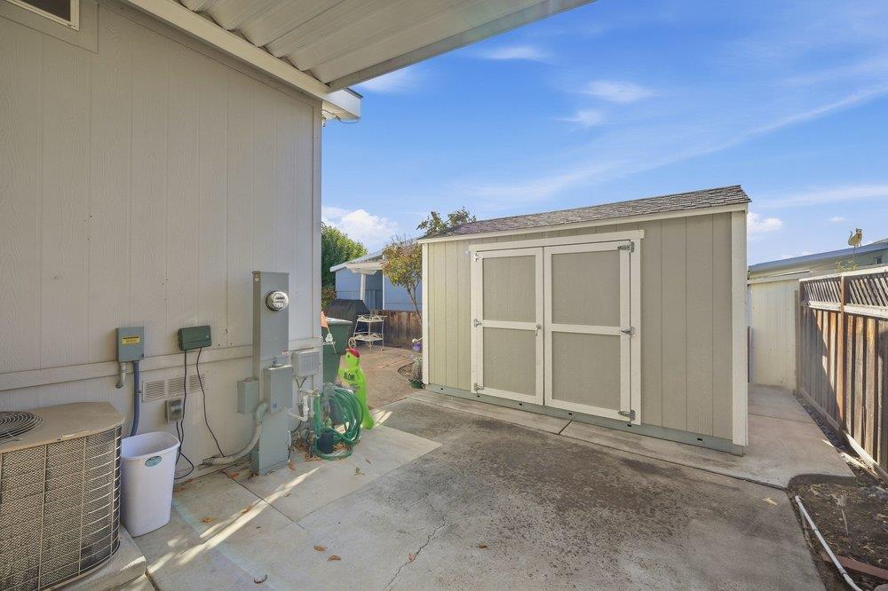 Detached beige storage shed in a concrete side yard beside the house.