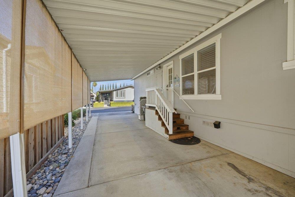 Covered walkway beside a home, with wooden entrance steps and a screened fence.