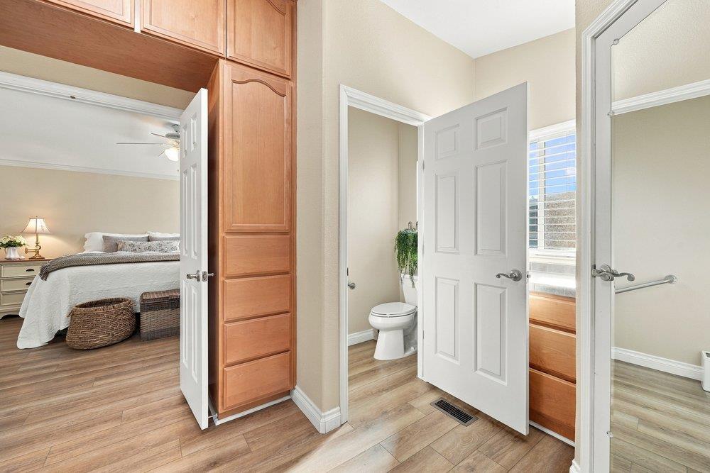 Bathroom with built-in wood cabinetry and a toilet, adjoining a bedroom with a made bed.