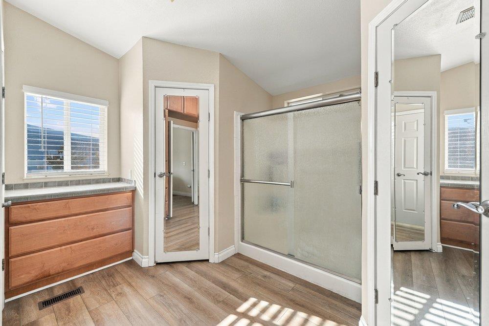 Bathroom with a wood vanity, frosted-glass shower, mirrored doors, and wood-look flooring.