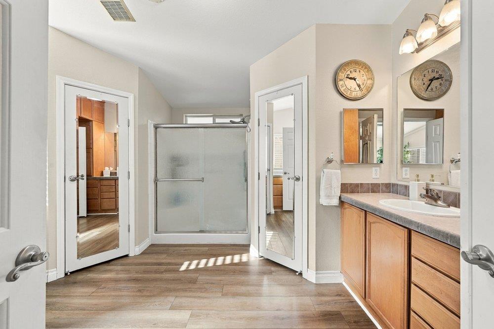 Bathroom with a frosted-glass shower, wood vanity, and wood-look tile flooring.