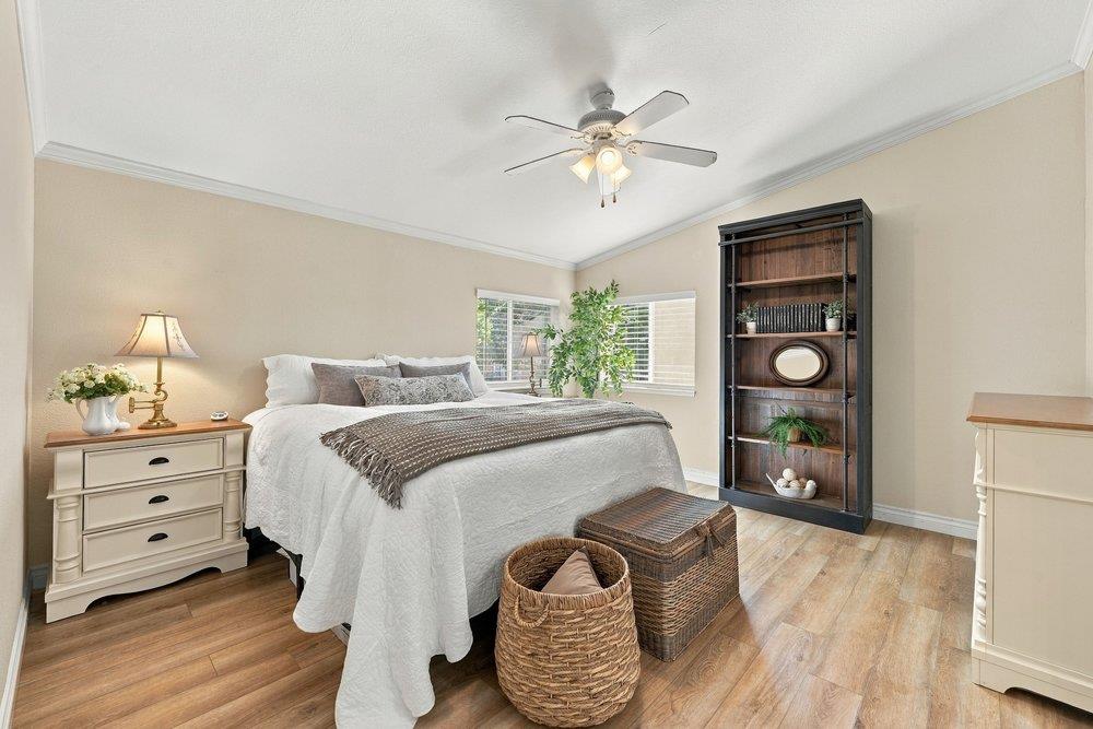 Staged bedroom with a white bed, tall dark bookcase, woven baskets, and ceiling fan.
