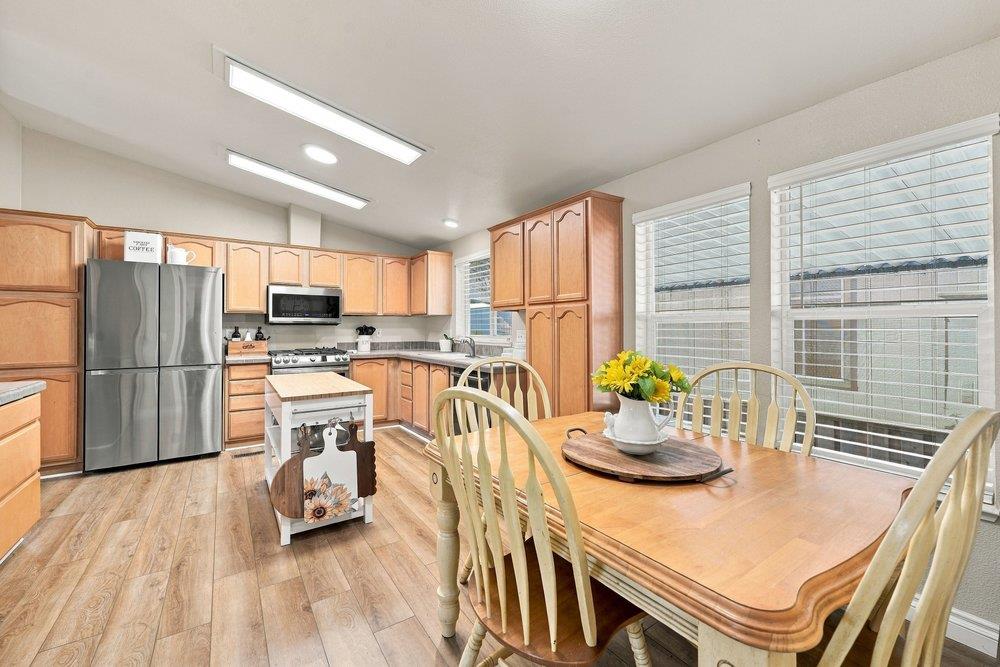 Kitchen and dining area with light wood cabinets, stainless steel appliances, and a large table by the windows.