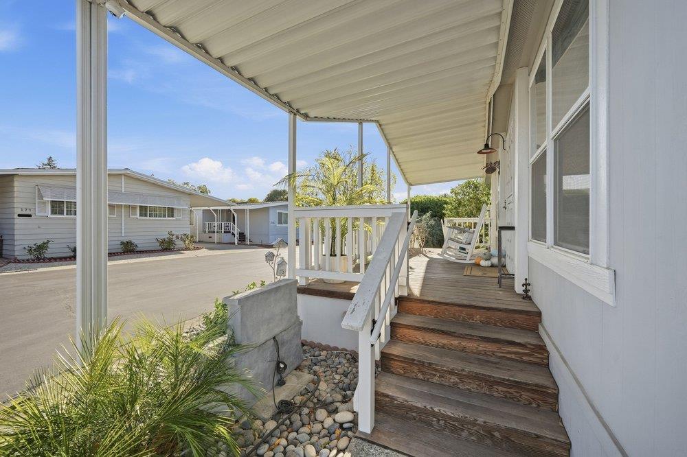 Covered front porch with wooden steps, white railing, and a porch swing beside a landscaped stone bed.