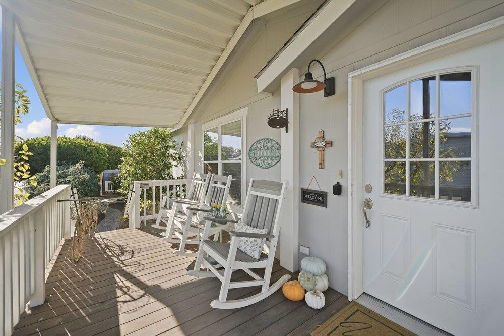 Covered front porch with white rocking chairs, wood decking, and pumpkins beside the entry door.