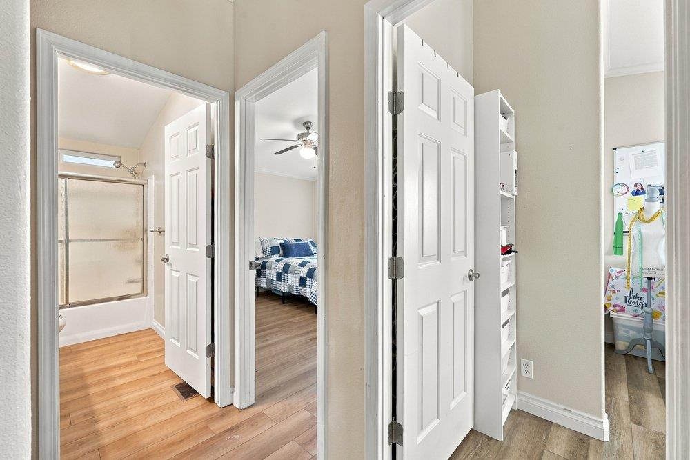 Hallway with open doors to a bathroom and bedroom, featuring wood-look floors and a blue-and-white quilt.