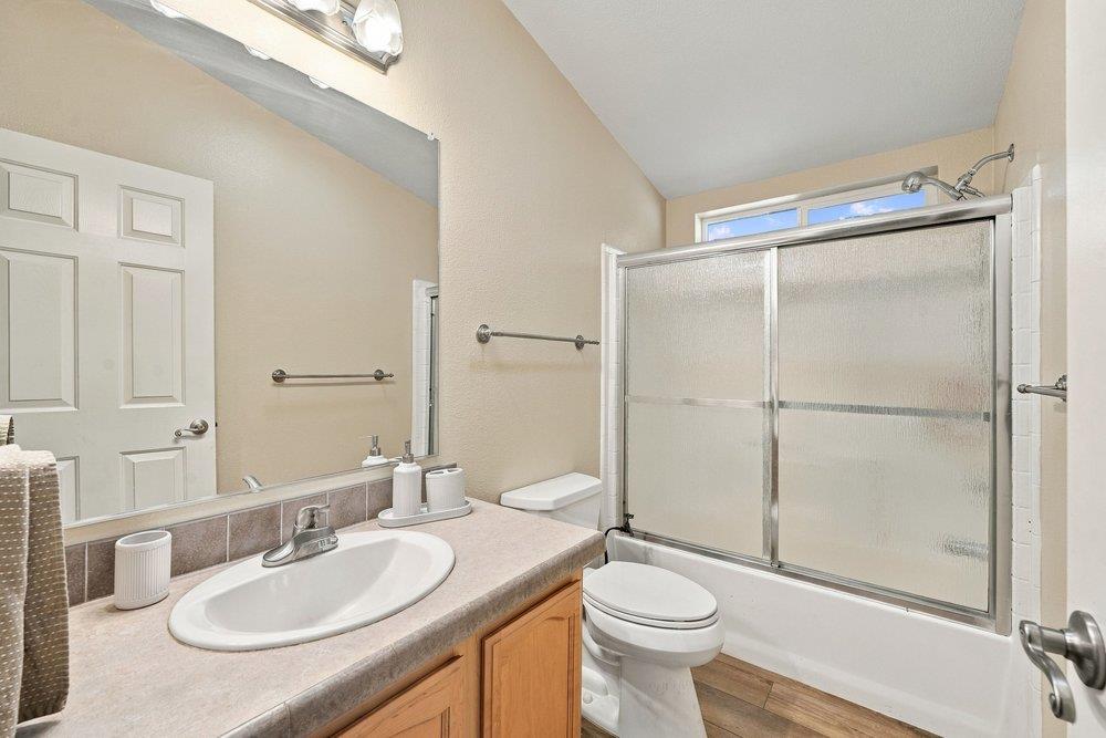 Bathroom with a wood vanity, oval sink, and bathtub with sliding frosted-glass doors.