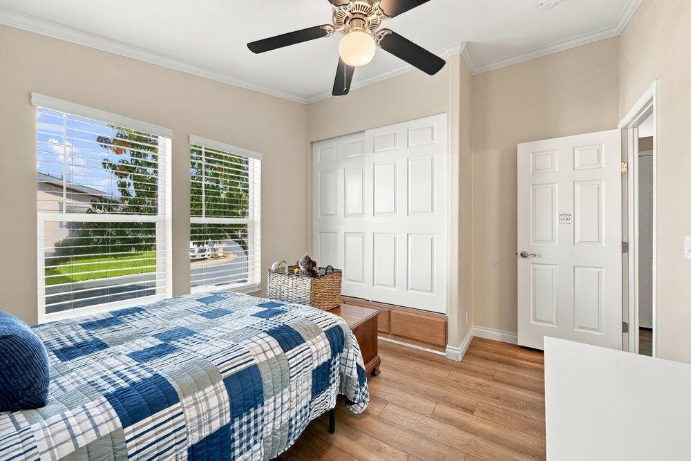 Bedroom with a blue-and-white patchwork bedspread, two shuttered windows, and hardwood floors.