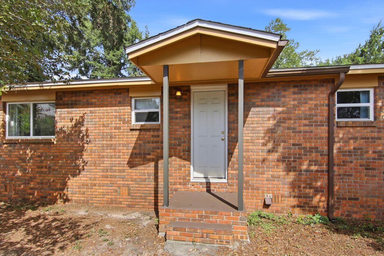 Brick house entrance with a white door beneath a projecting covered porch.