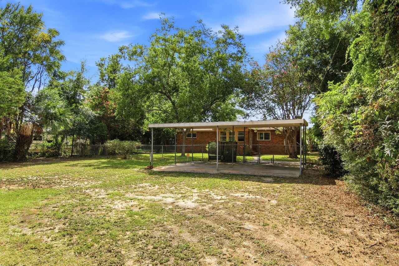 Brick house behind a metal-roofed carport, surrounded by mature trees and a spacious yard.
