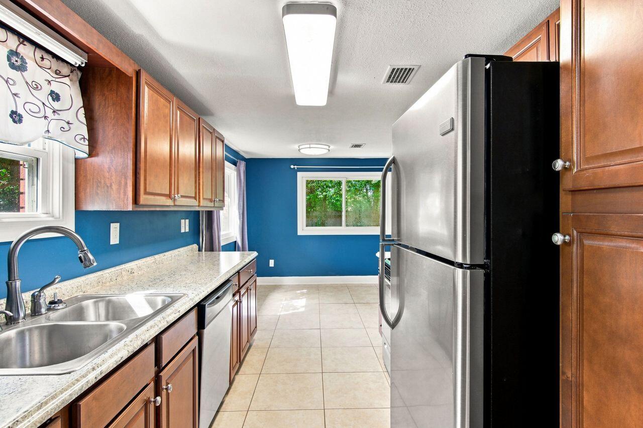 Kitchen with warm wood cabinets, blue walls, granite counters, and a stainless-steel refrigerator.