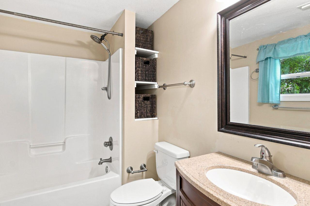 Bathroom with a white tub and shower, built-in basket shelves, and a dark wood vanity.
