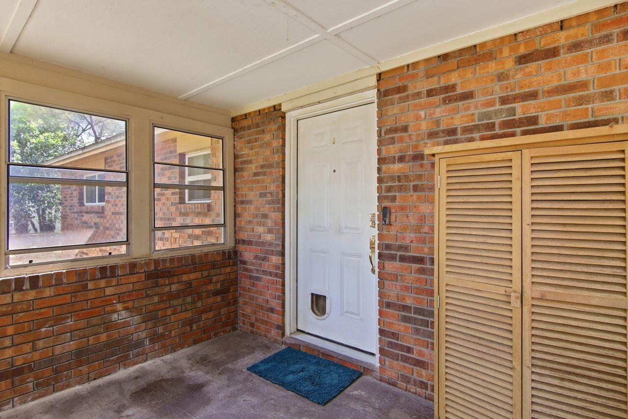 Covered brick entry with a white door, two windows, and a louvered wooden cabinet.