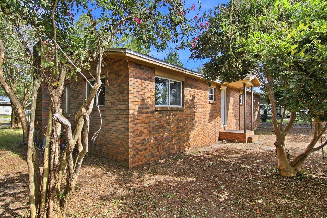 Single-story brick house with a covered entry porch, framed by mature trees.