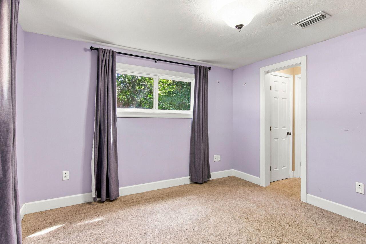Empty bedroom with lavender walls, beige carpet, and a curtained window.