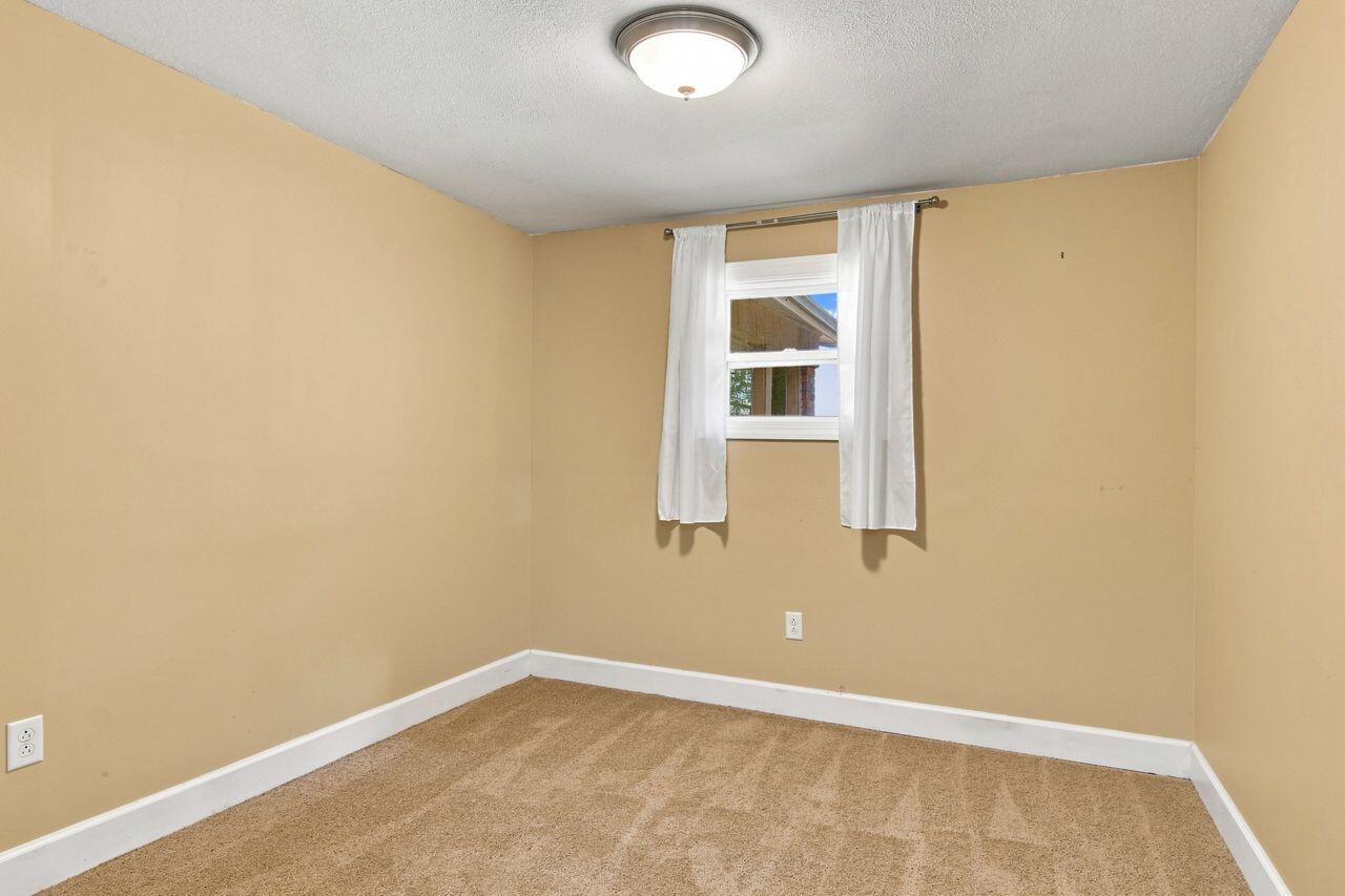 Empty bedroom with tan carpet and a small curtained window.