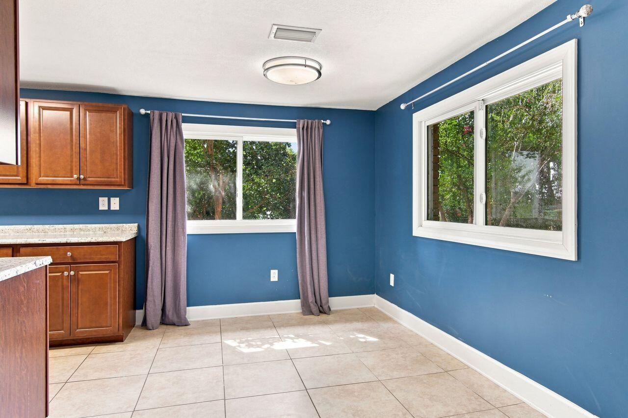 Kitchen with wood cabinets, blue walls, curtained windows, and light tile flooring.