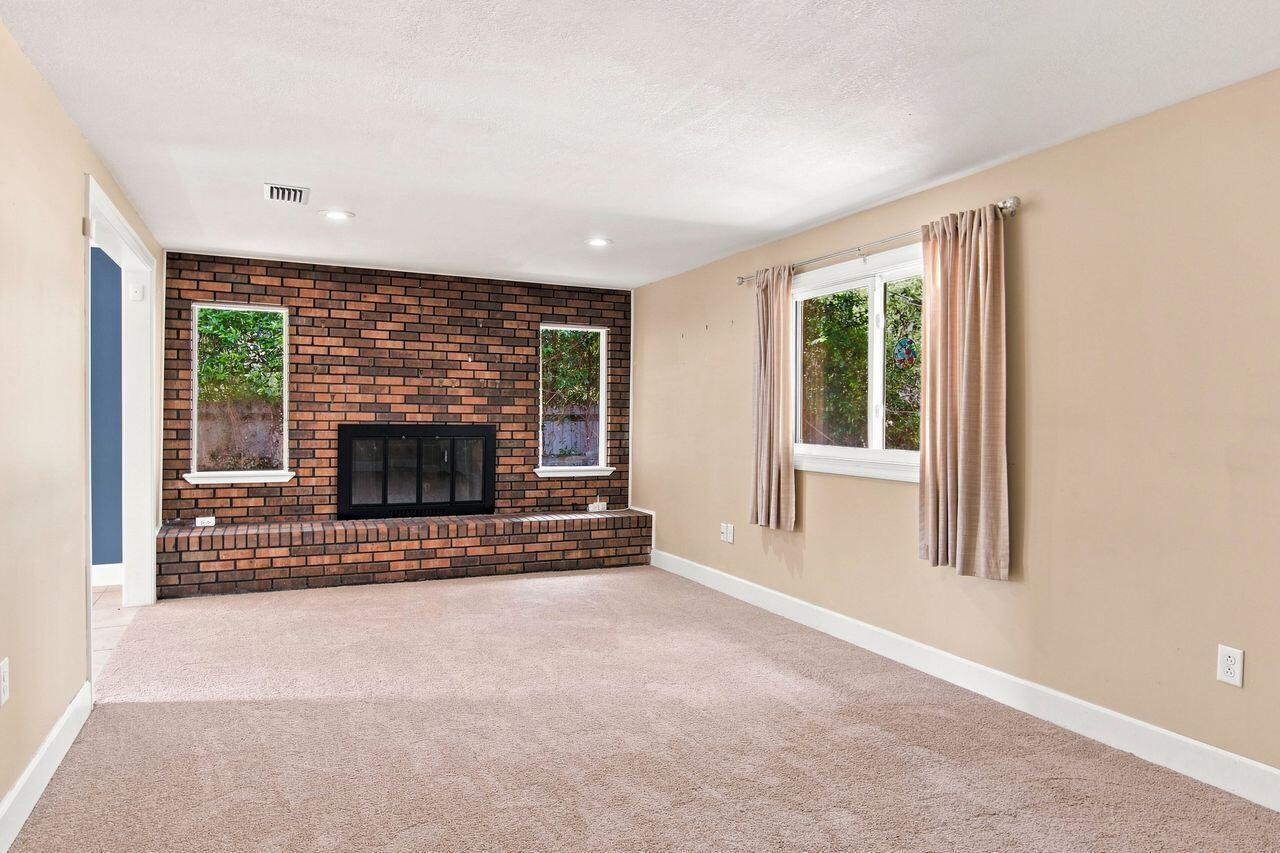 Empty living room with a brick fireplace, raised hearth, and curtained windows.
