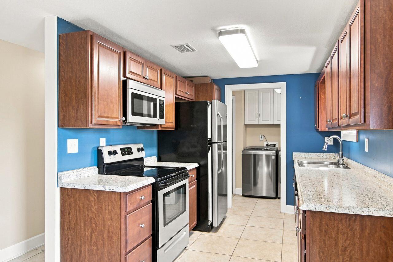 Galley kitchen with blue walls, wood cabinets, speckled counters, and a washer at the rear.