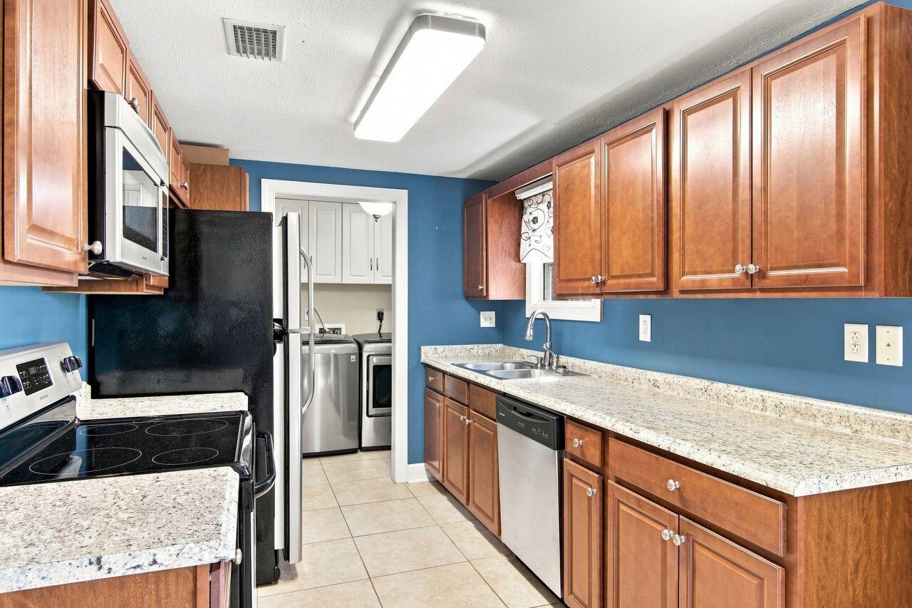 Kitchen with wood cabinets, blue walls, stone counters, and a doorway to the laundry area.