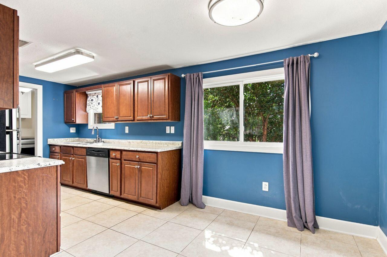 Kitchen with dark wood cabinets, stainless dishwasher, blue walls, and a large curtained window.