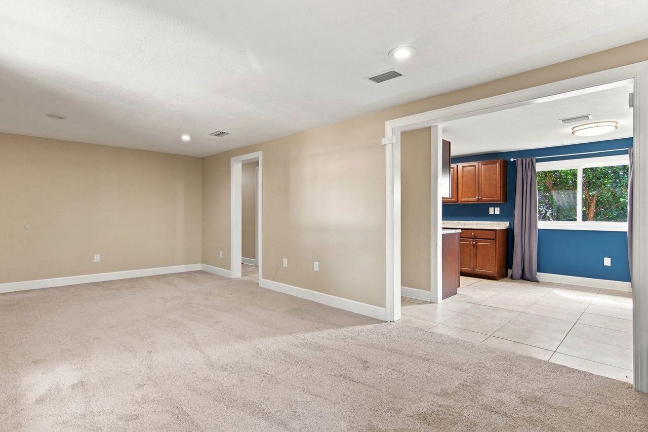 Empty carpeted living room opening to a blue-walled kitchen with wood cabinets.